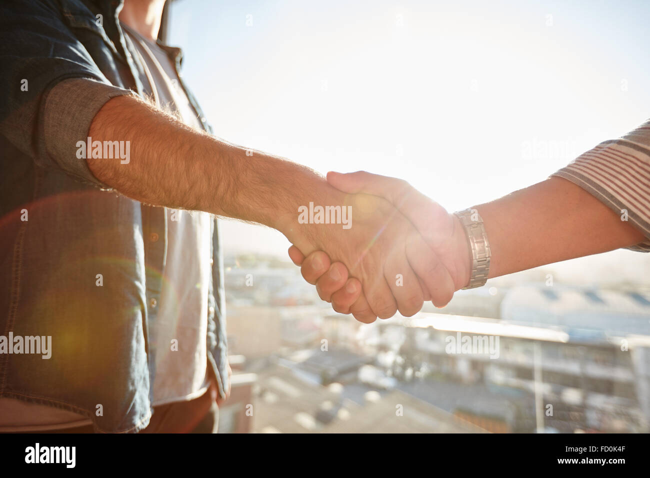 Closeup of two shaking male hands with sun flare. Focus on handshake against cityscape. Stock Photo