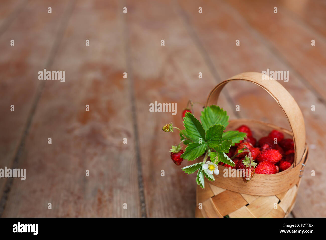 Basket with ripe berries (strawberries) on the background of the wooden floor Stock Photo