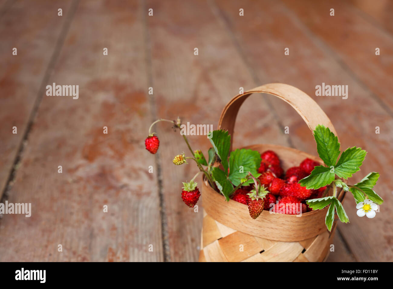 Basket with ripe berries (strawberries) on the background of the wooden floor Stock Photo