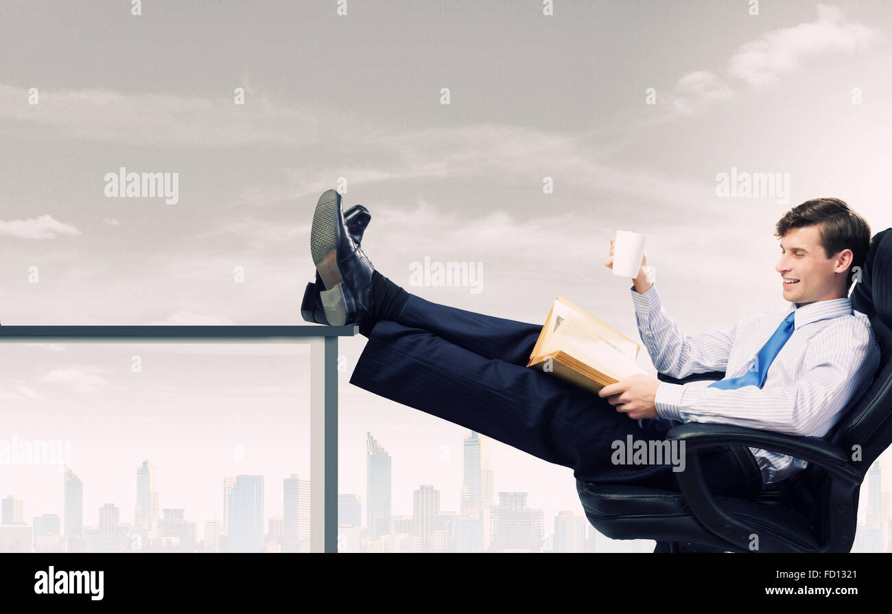 Smiling businessman sitting in chair with legs on table Stock Photo - Alamy
