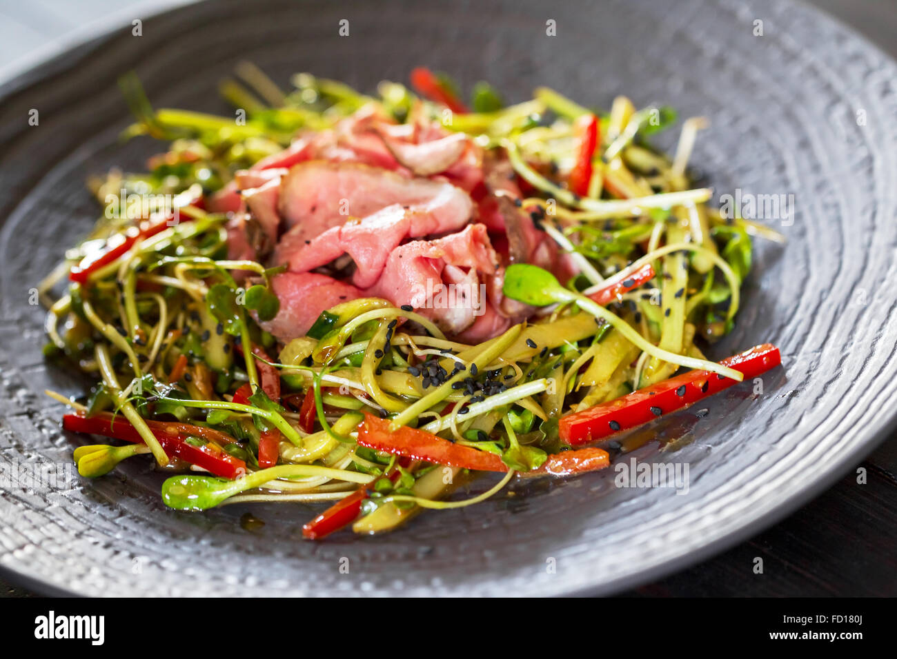 Authentic salad with bacon fresh red pepper, sprouts, sesame and olive oil on a black plate