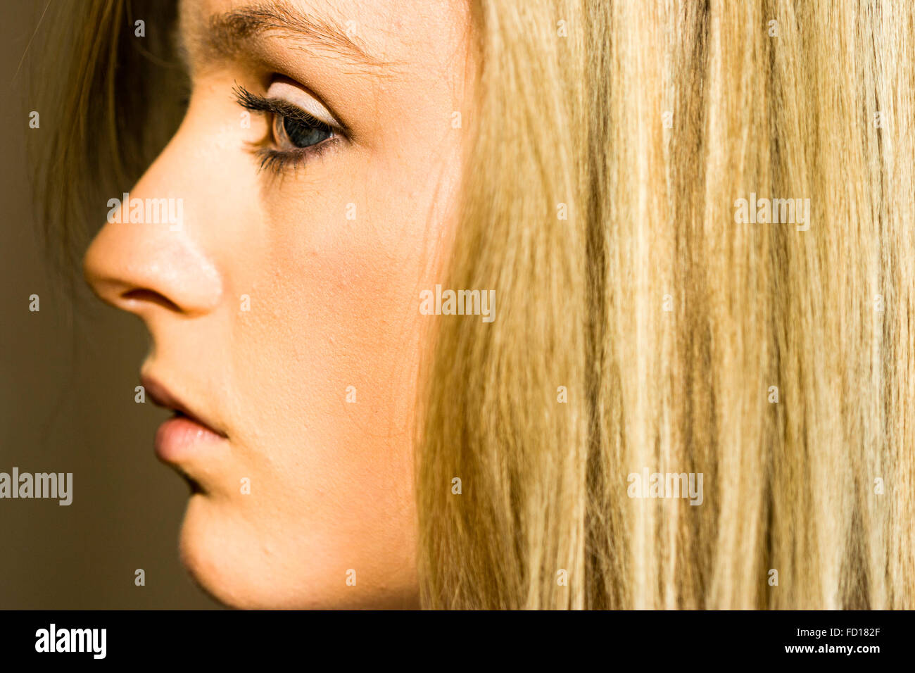 Caucasian teenage girl with blue eyes. Close up of face, side profile. Annoyed angry expression, long blonde straight hair. Focus on eye. Stock Photo