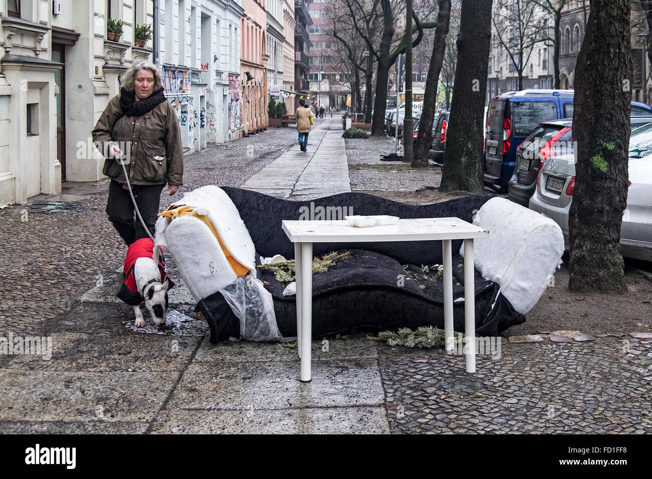 Passersby  and dog stare at discarded furniture, sofa and table on a Berlin pavement Stock Photo