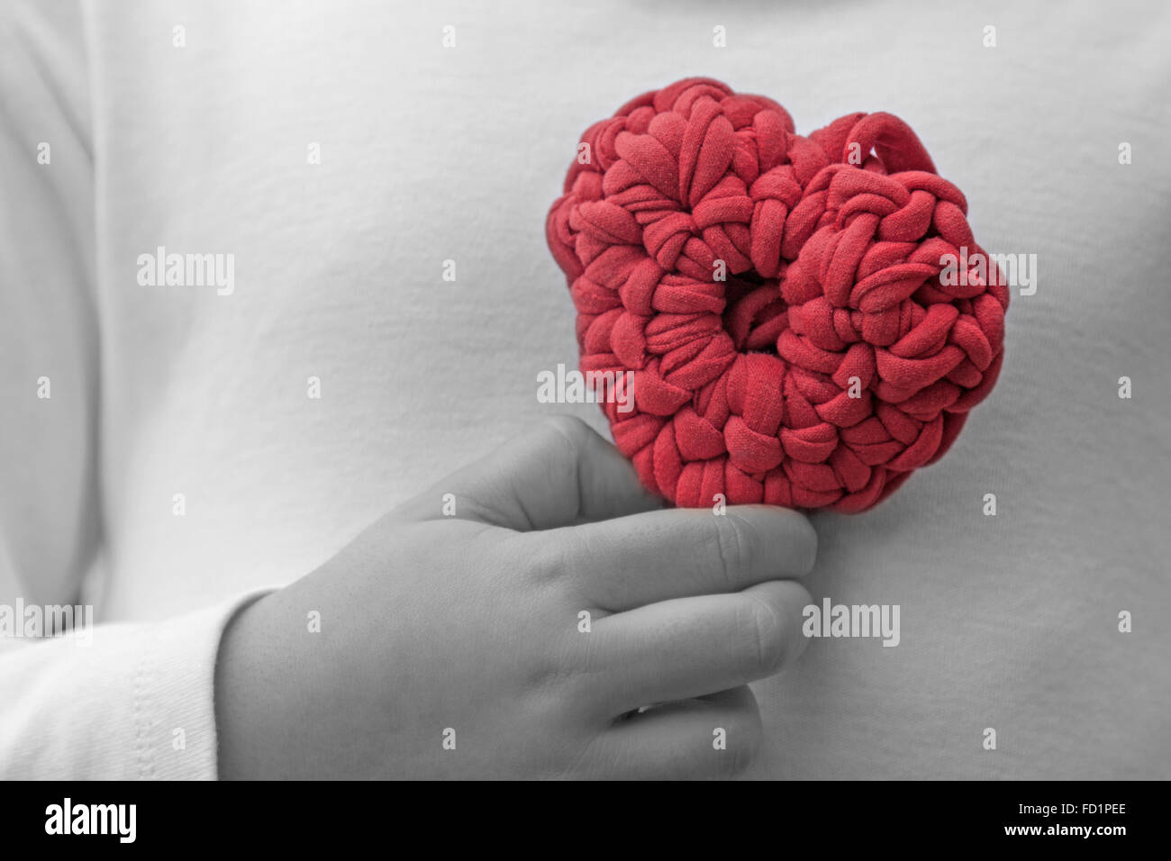 a horizontal frontal view of a crochet heart being held by a little girl on her chest with space for a message Stock Photo