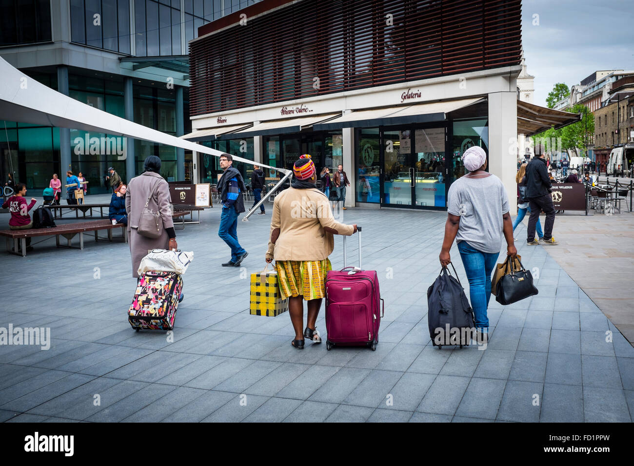 Three black women pulling luggage with wheels in the street of London, UK Stock Photo