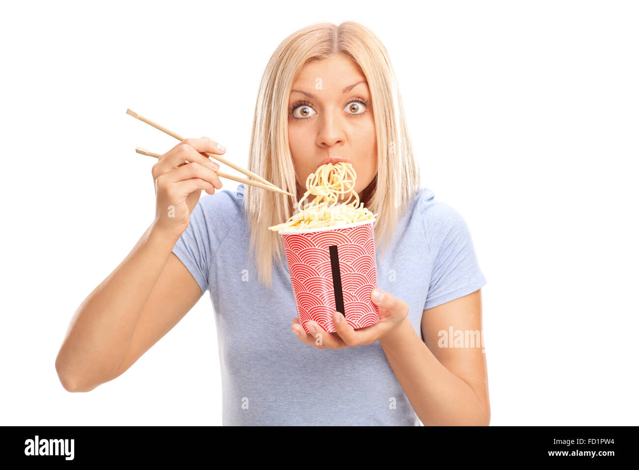Surprised young woman eating Chinese noodles and looking at the camera
