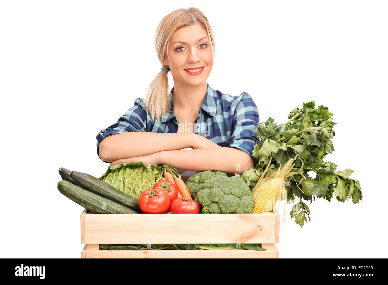 Young woman posing behind a wooden crate full of fresh vegetables ...