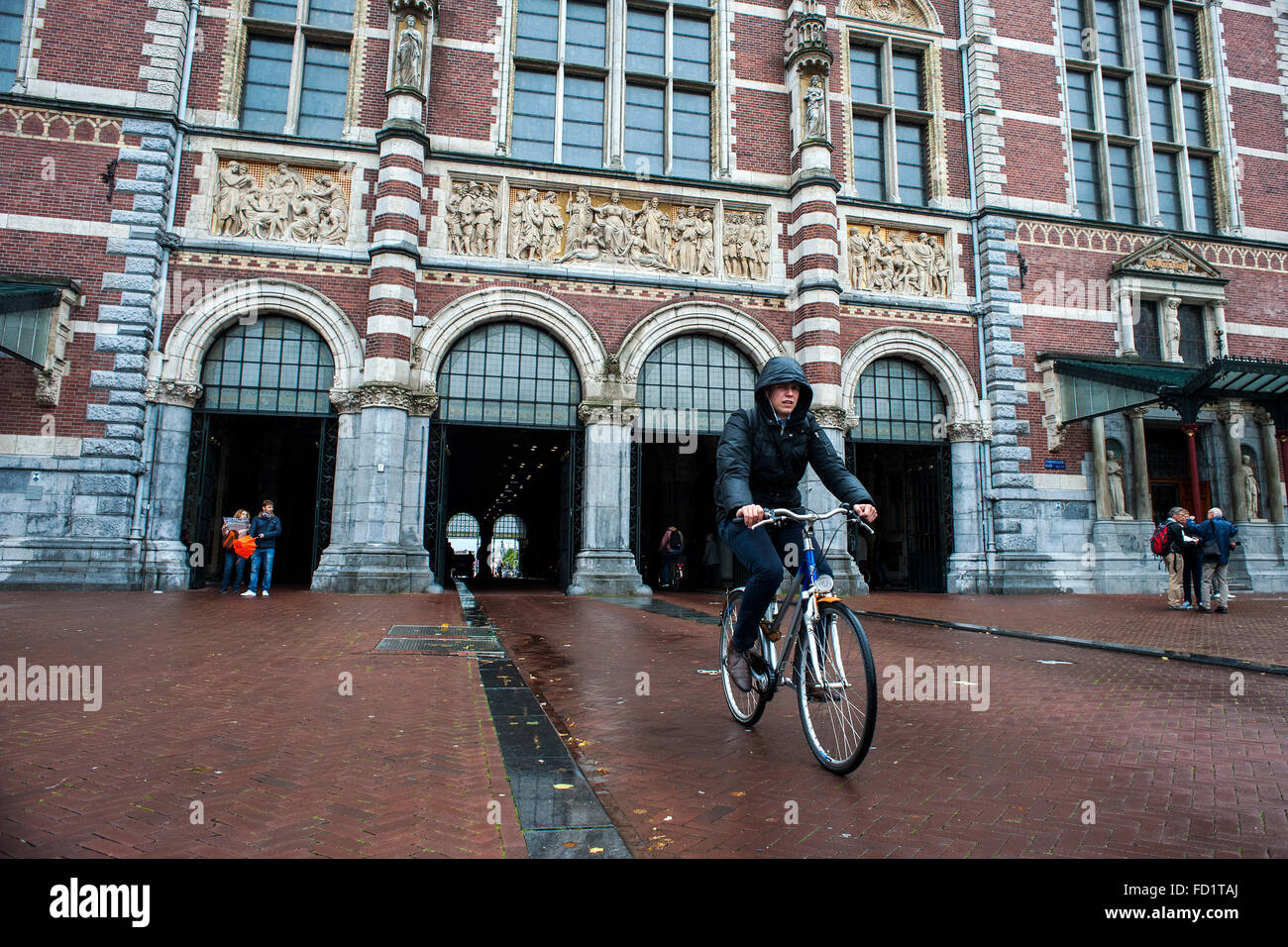 A young woman spends a bike in front of the entrance to the Rijksmuseum one of the architectural jewels of Amsterdam Stock Photo