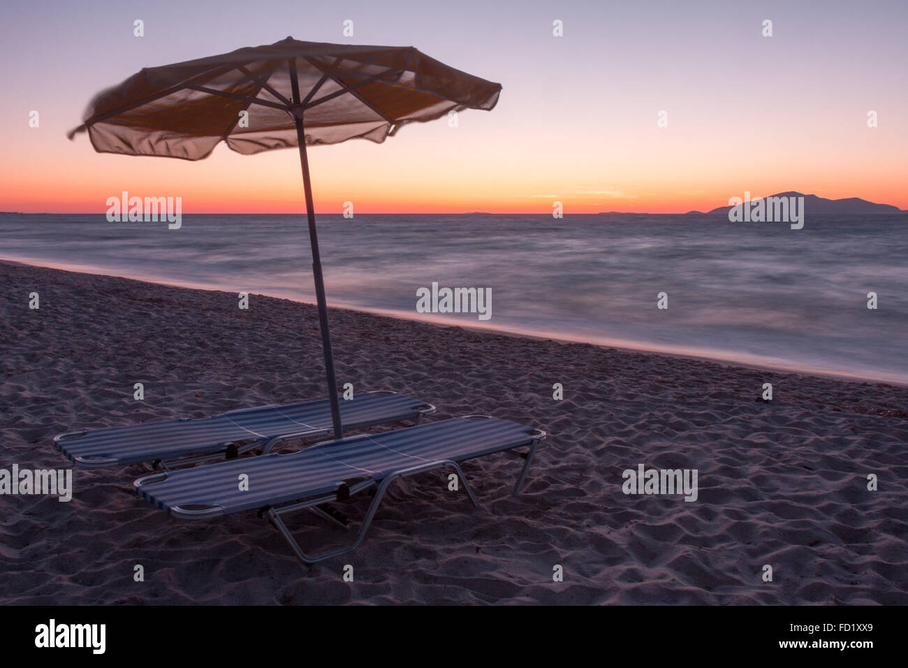 long exposure at dusk on beach with parasol in foreground and island of Kalimnos in the background Stock Photo