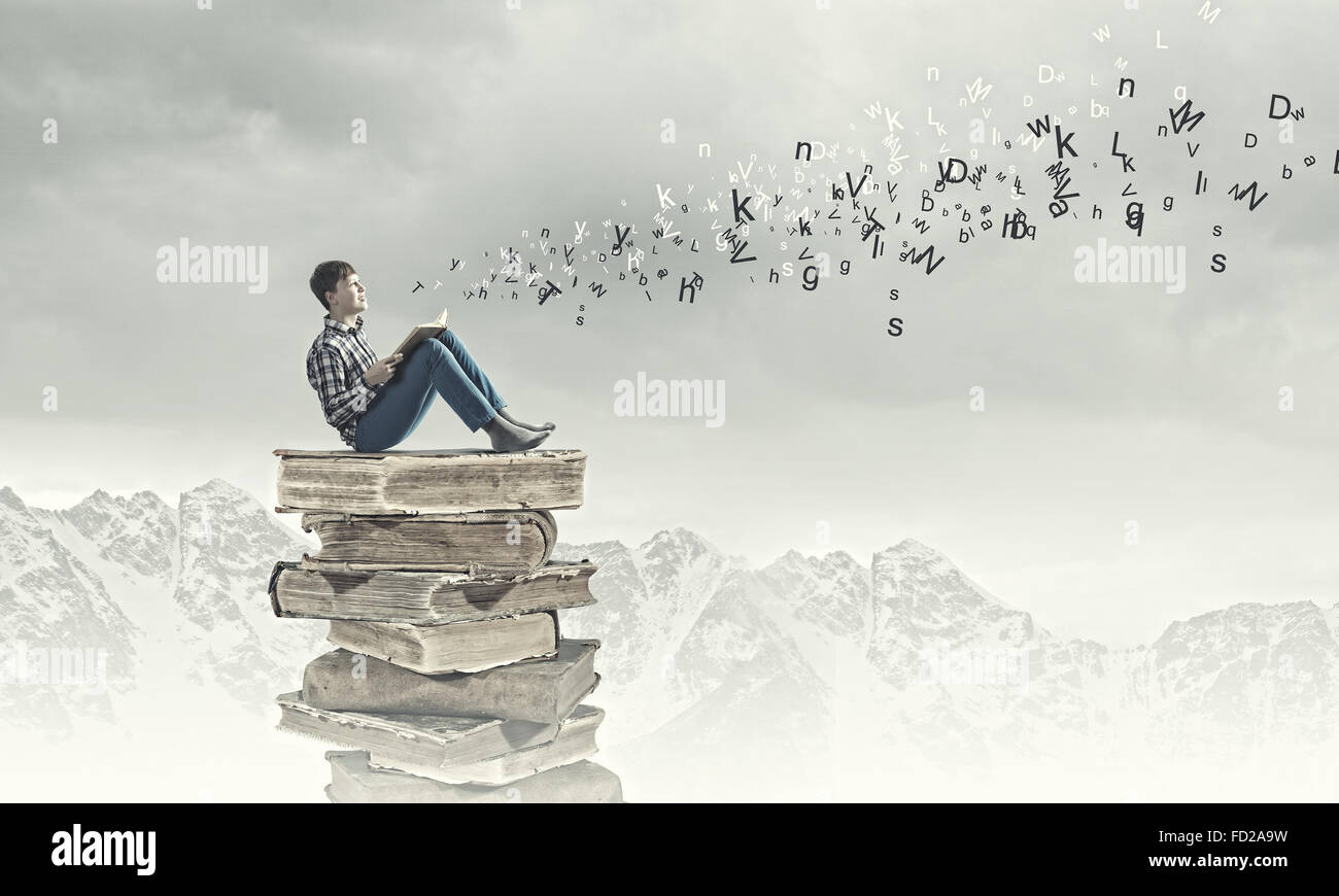 Teenager sitting on pile of books and reading Stock Photo - Alamy
