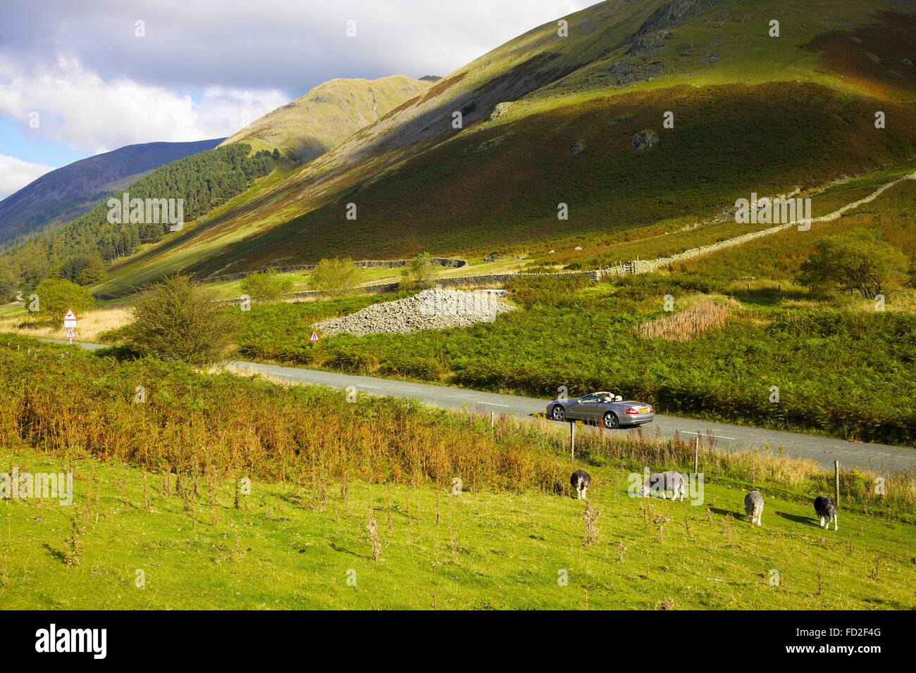 Car crossing Dunmail Raise. Mountain pass with cairn which was raised over the body of King Dunmail, the last king of Cumbria. Stock Photo