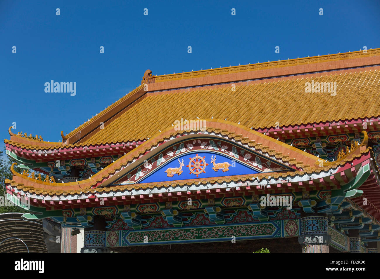 Colourful red tiled roof. Chinese temple roof lined with light bulbs with blue facia decorated with religious symbol. Stock Photo