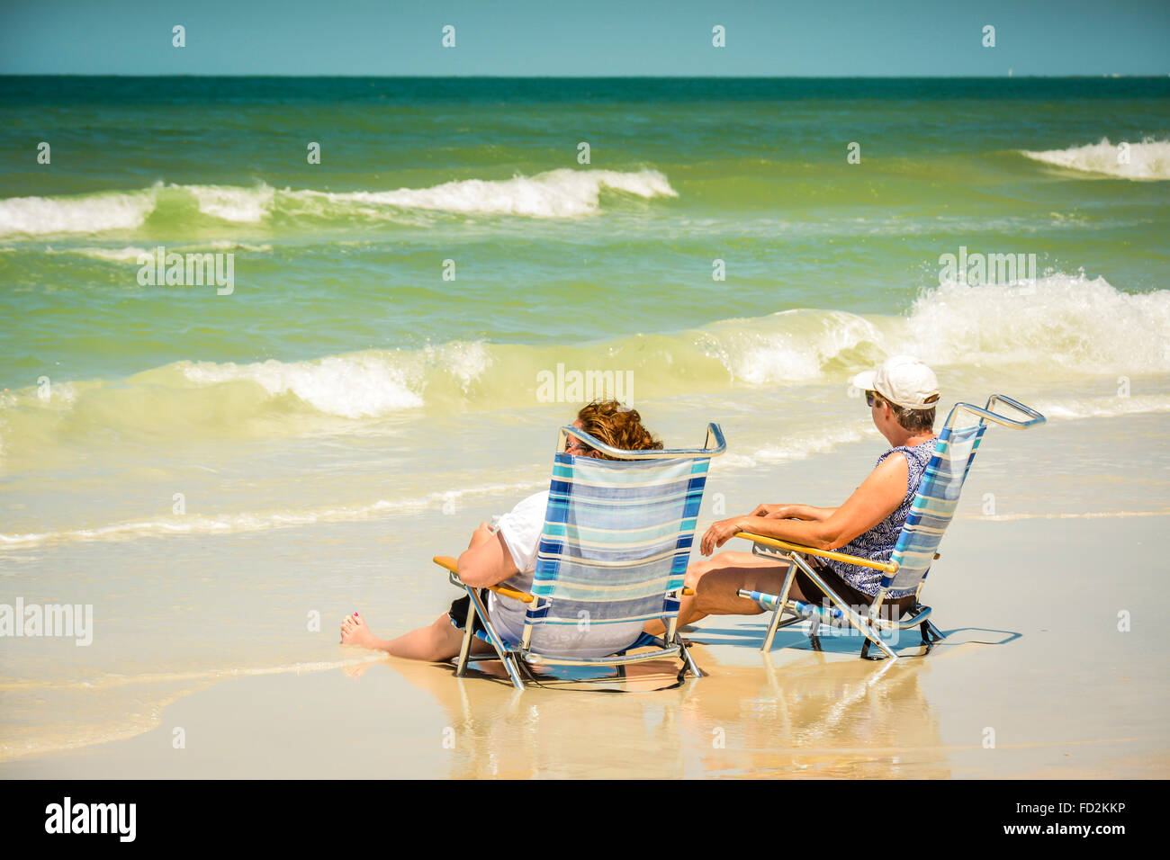 Two women enjoy sitting in their beach chairs with their legs in the surf at the shoreline and watching the waves roll in Stock Photo