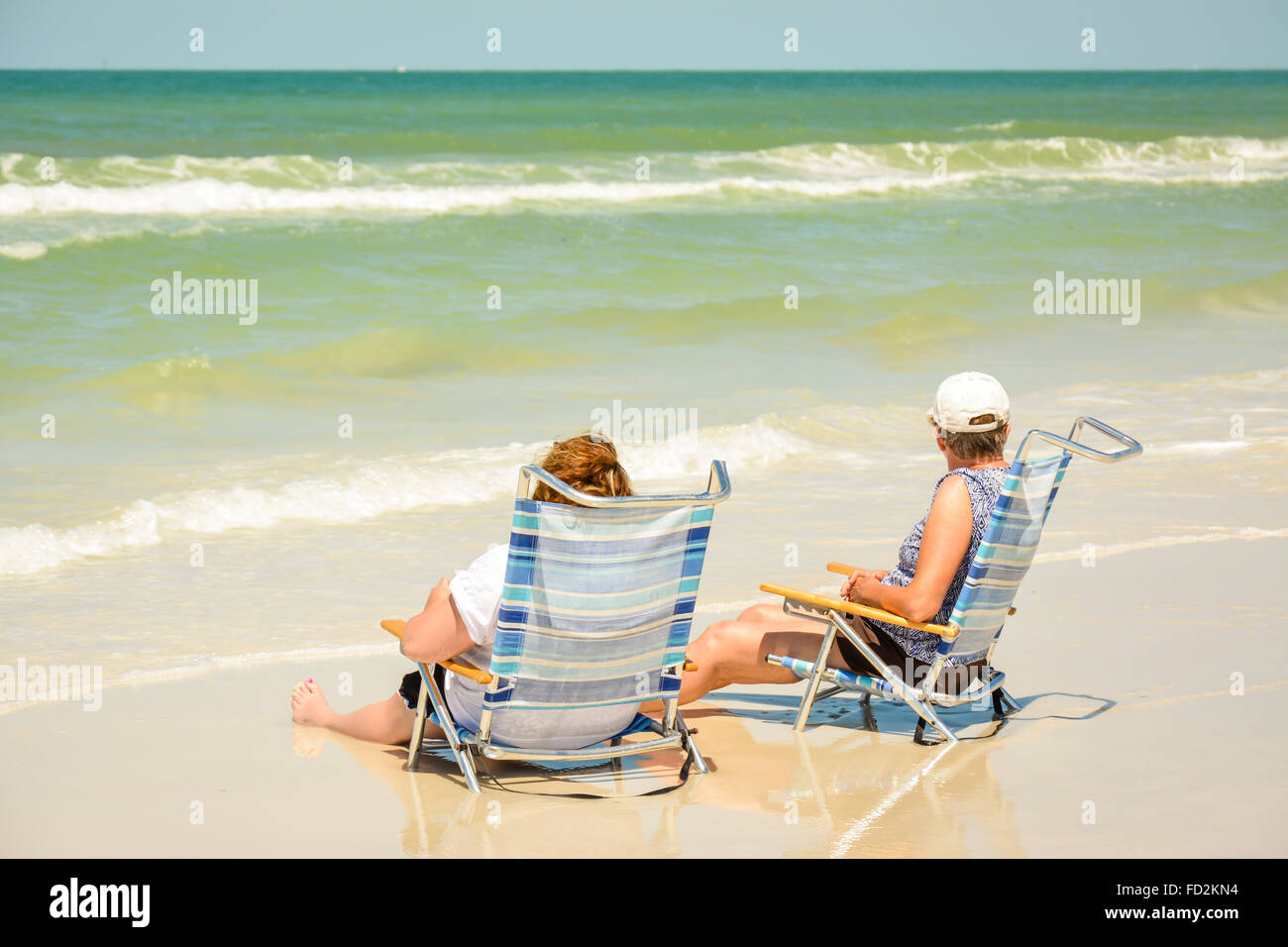 Two women enjoy sitting in their beach chairs with their legs in the surf at the shoreline and watching the waves roll in Stock Photo