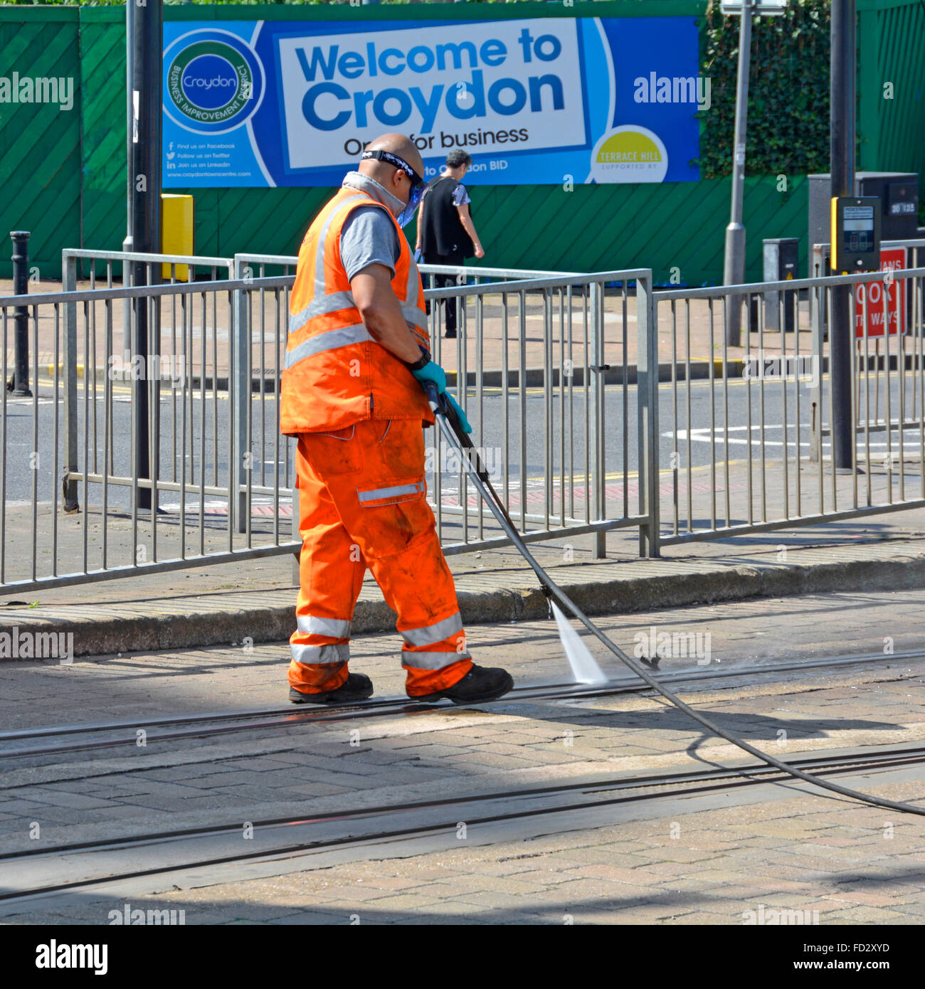 Man pressure washing tram points in Croydon Tramlink tracks in road with 'Welcome to Croydon' poster beyond London England UK Stock Photo