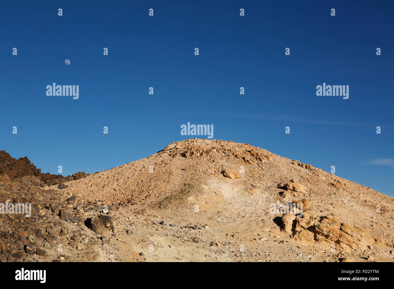 The moon rises above sulphur-laced rock on Mount Teide in Teide National Park on Tenerife, Spain. Stock Photo