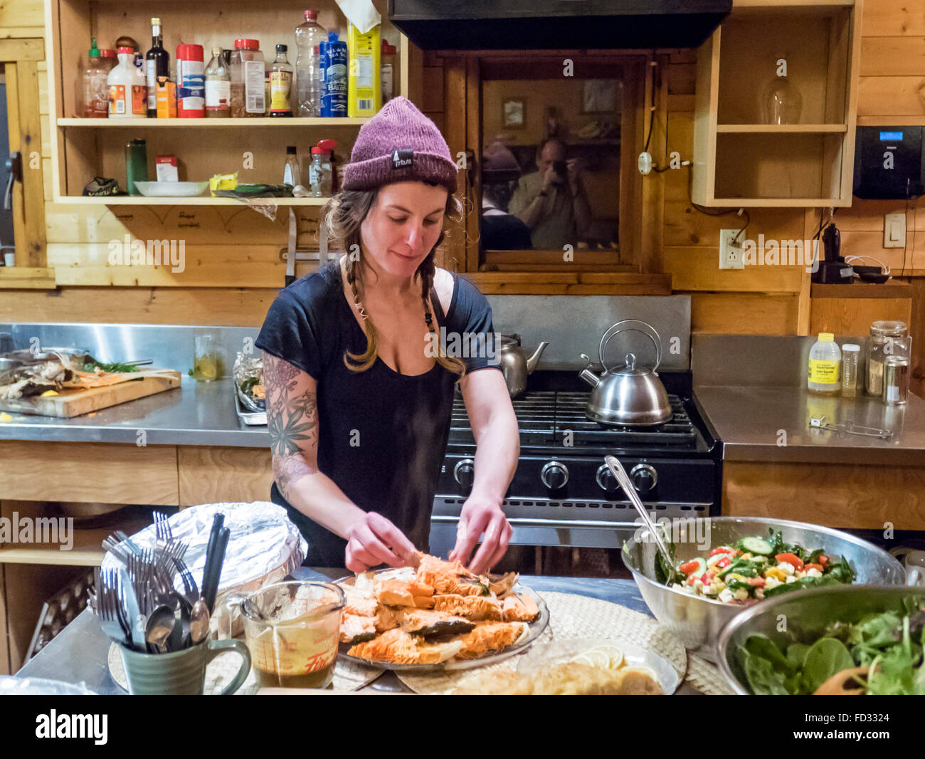 Young woman cooking for back country skiers inside remote Mount Carlyle Lodge; Selkirk Mountains; British Columbia; Canada Stock Photo