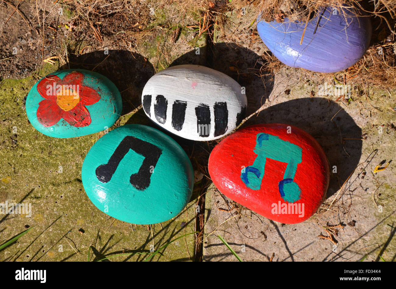 Colourful painted ornamental garden pebbles / rocks by children depicting flowers and musical notations Stock Photo