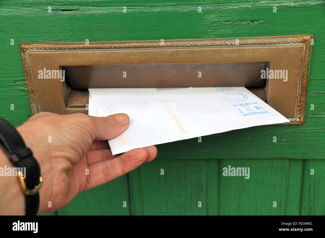 postman delivering a letter through a letter box of a wooden front door. Stock Photo