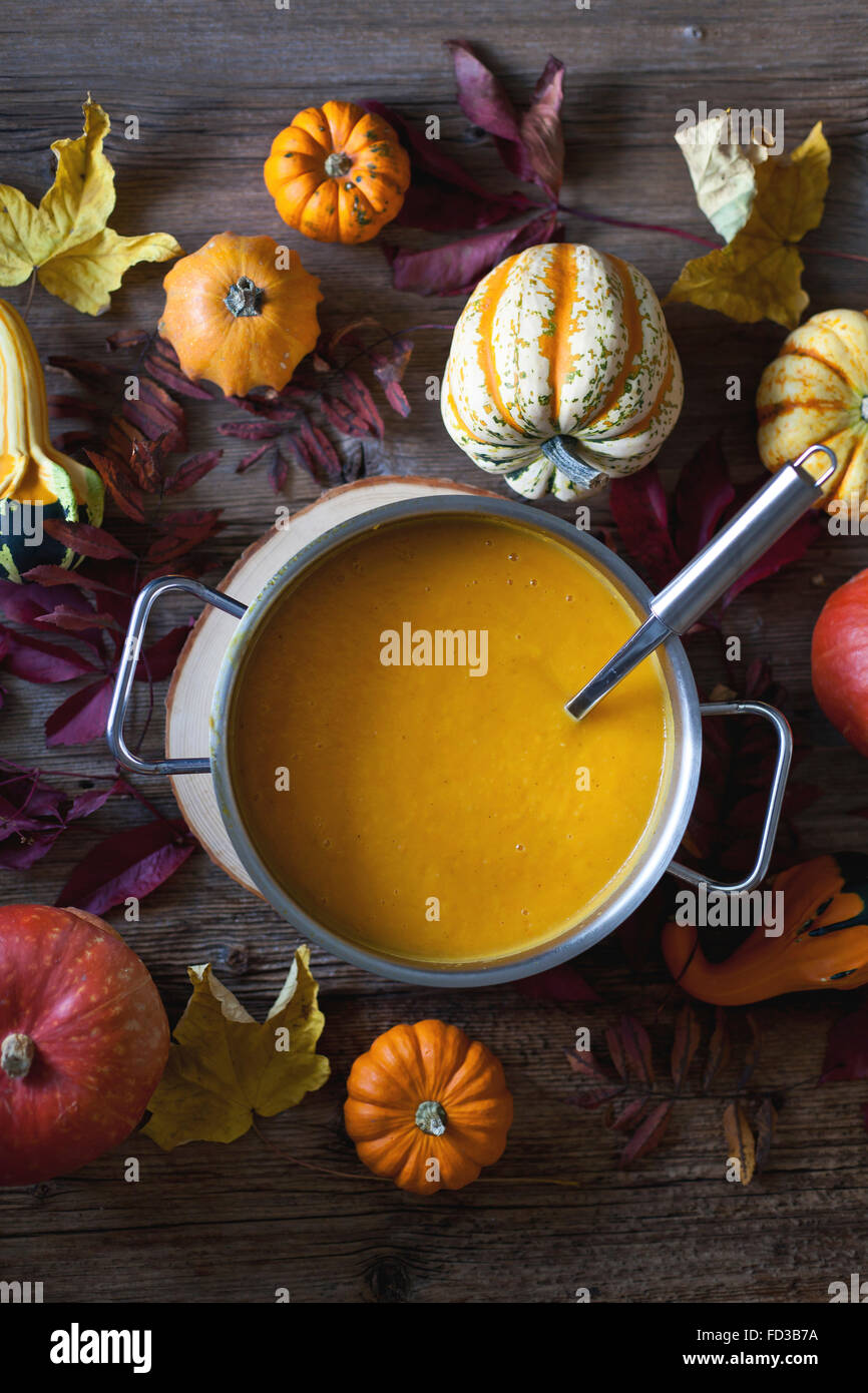 Pumpkin and sweet potatoes soup in a cooking pot, Autumn leaves and different pumkins varieties on a rustic wooden table Stock Photo