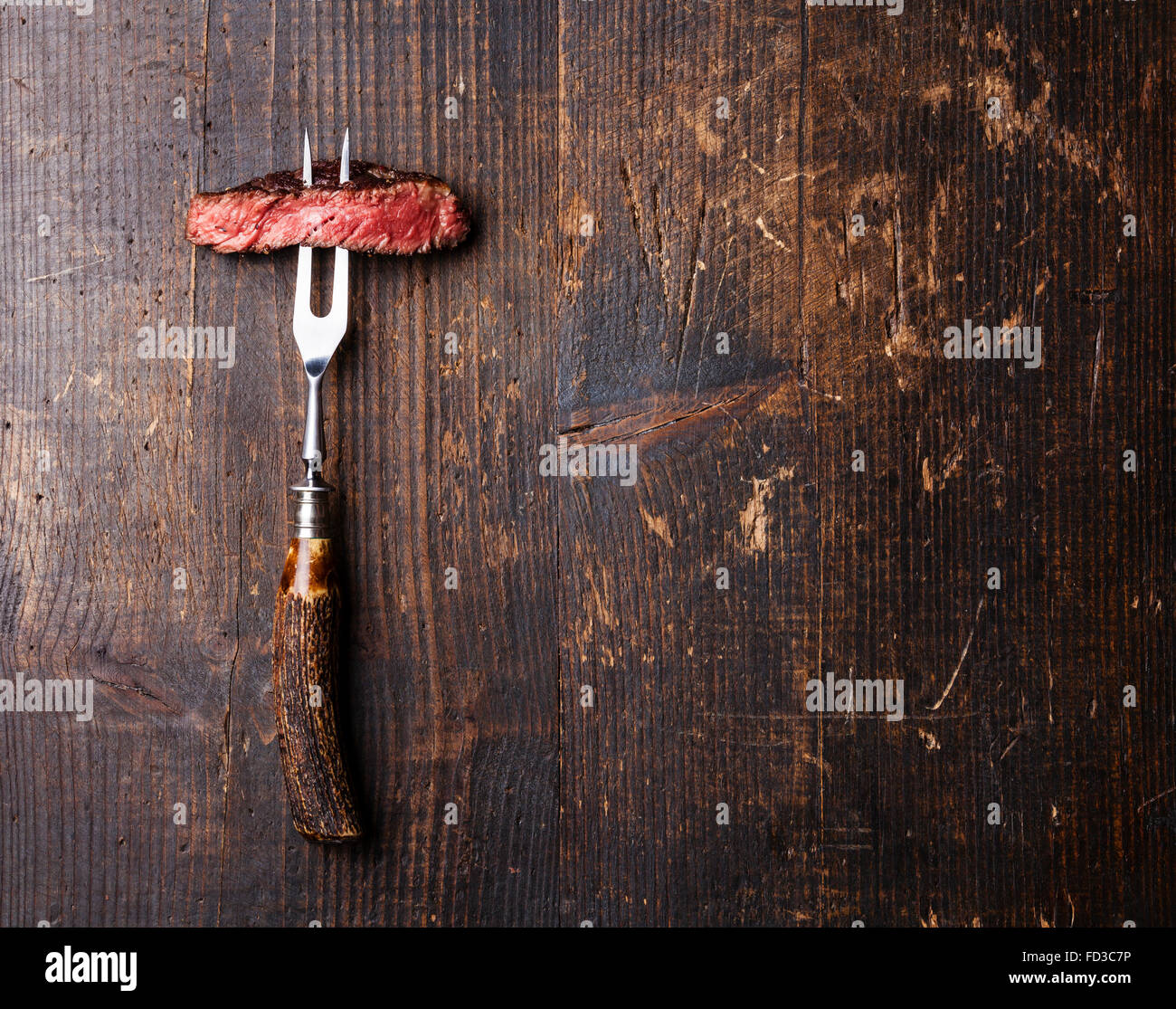 Slices of Medium rare grilled Steak Ribeye on meat fork on dark wooden