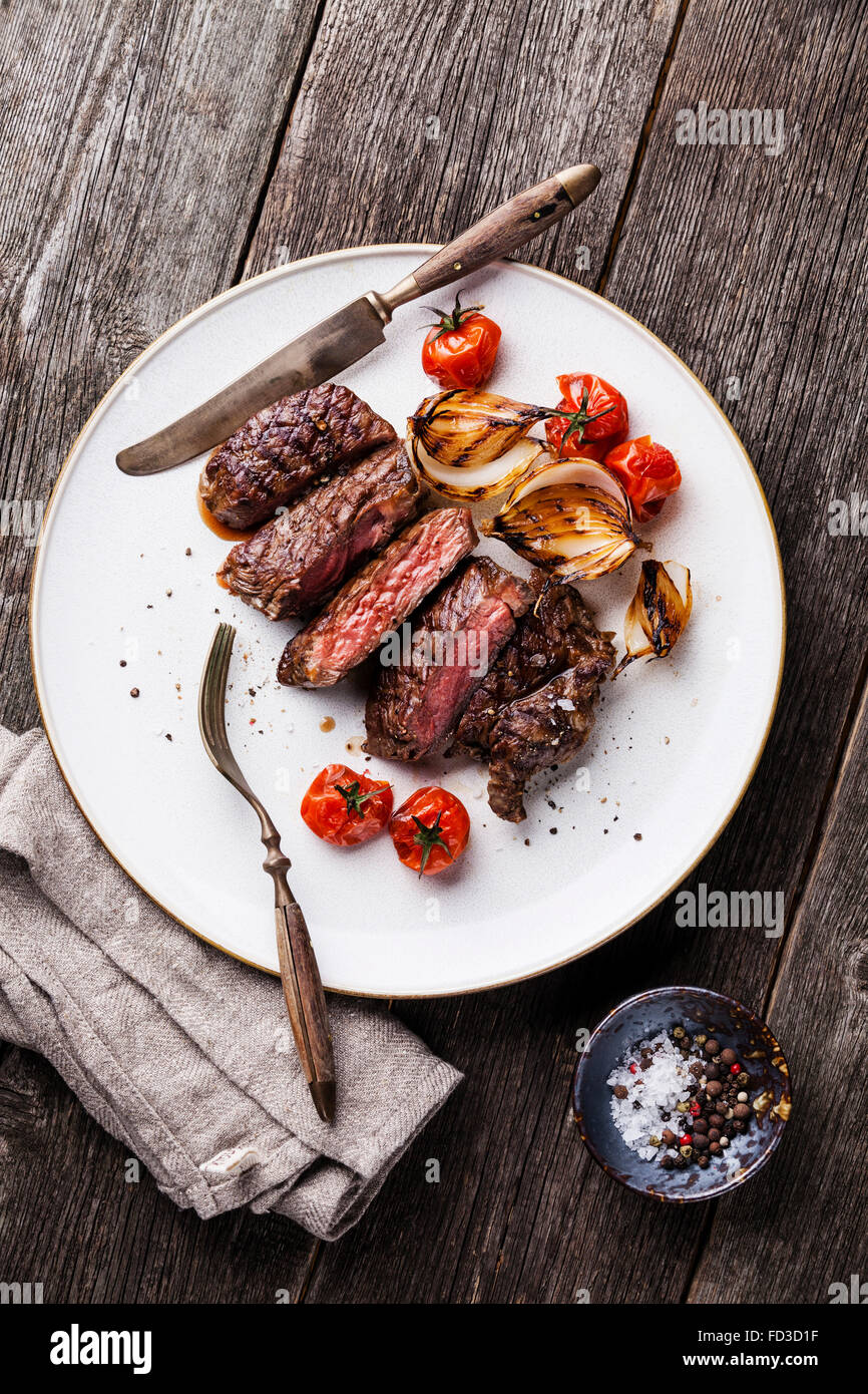 Sliced steak Ribeye with grilled onions and cherry tomatoes on plate on