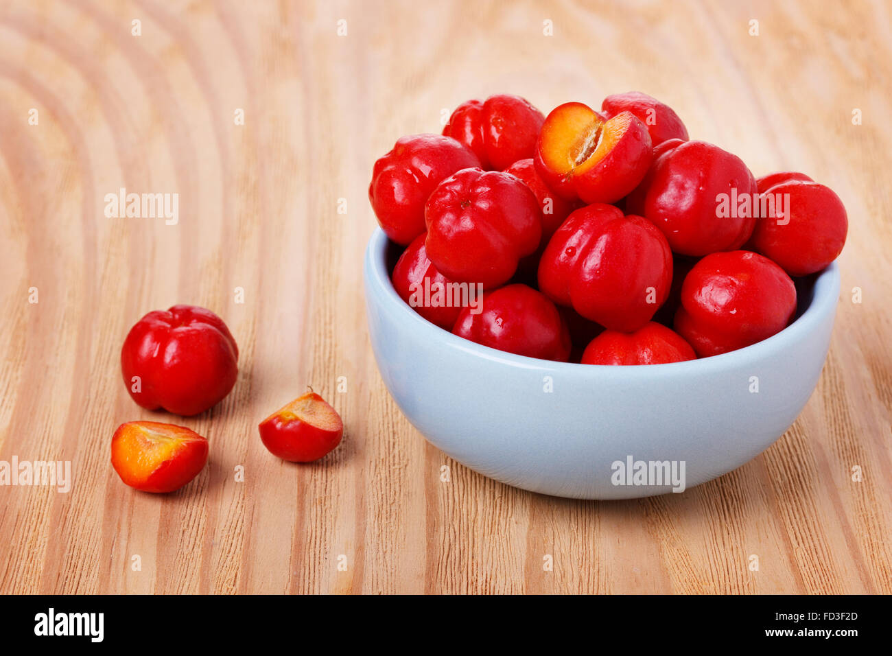 Malpighia glabra (red acerola), tropical fruit in bowl on wooden table. Selective focus Stock Photo