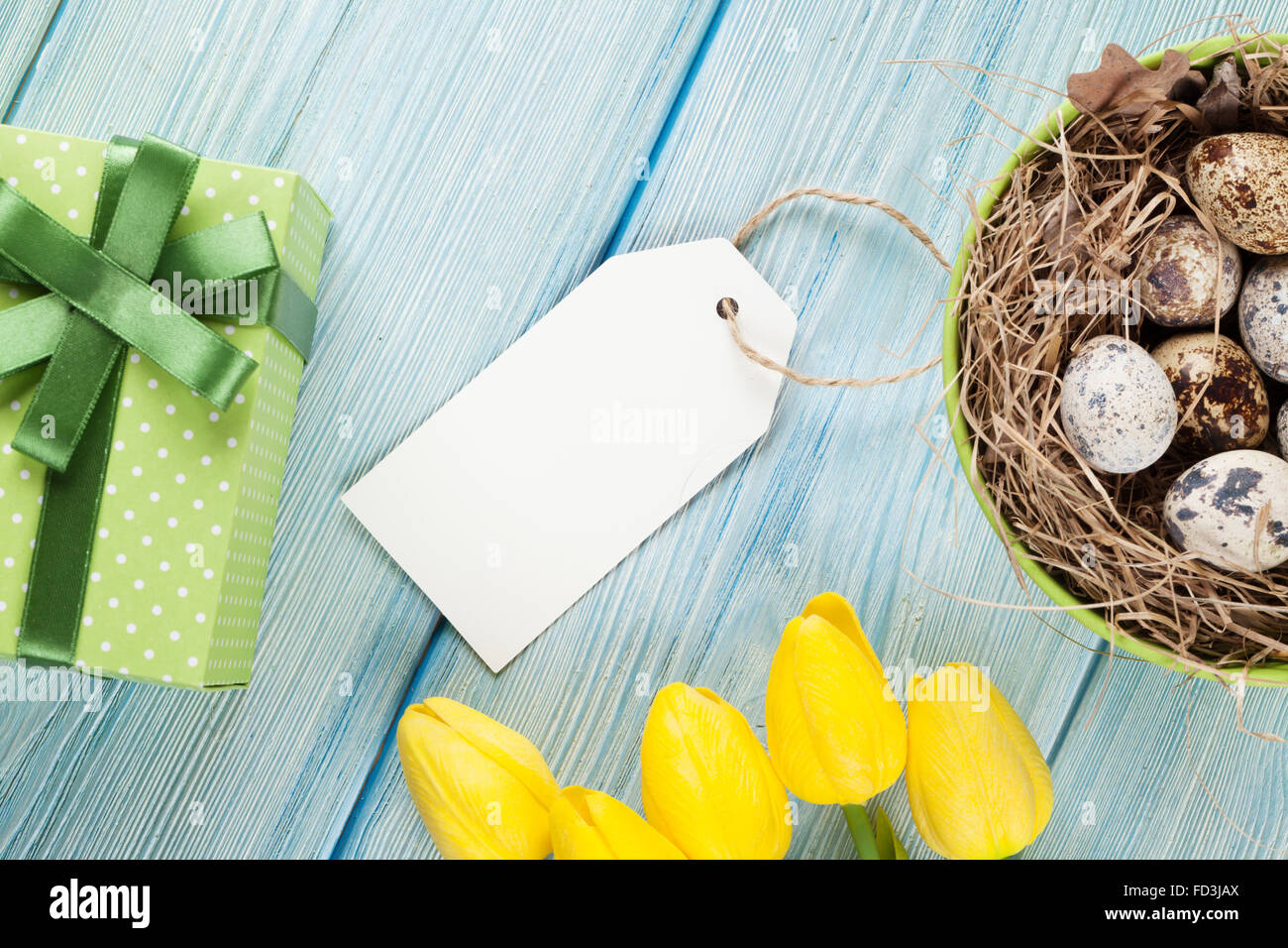 Easter with eggs in nest and yellow tulips over blue wooden table. Top ...