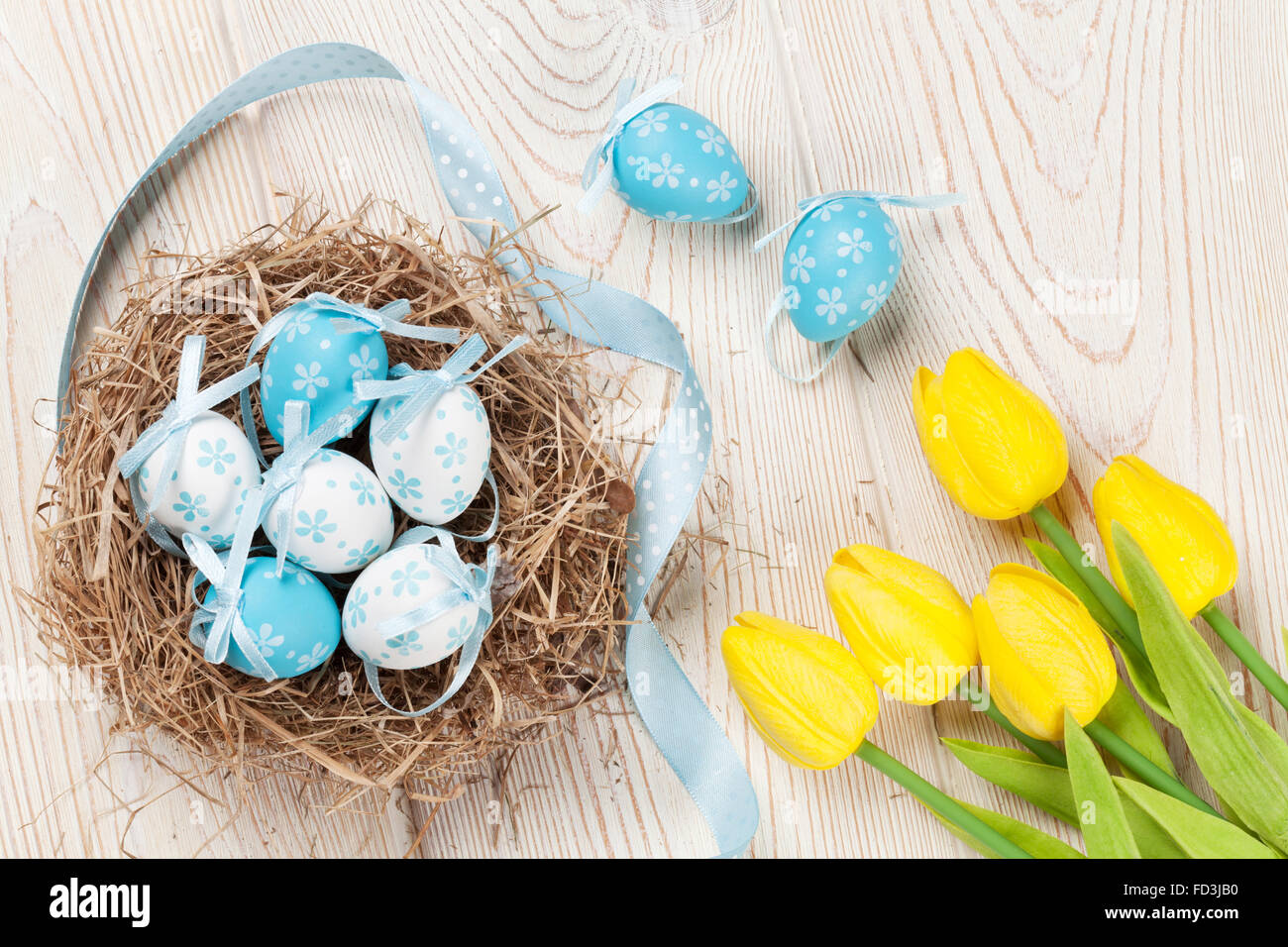 Easter background with eggs in nest and yellow tulips over white wooden ...
