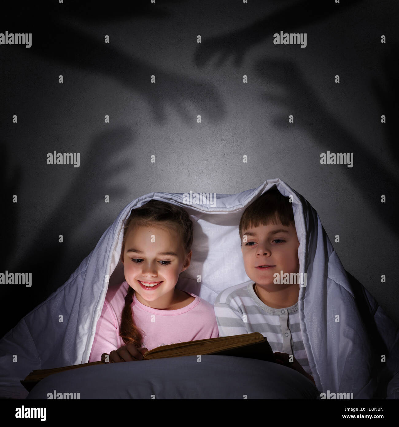 Children sitting in bed under blanket with book Stock Photo Alamy