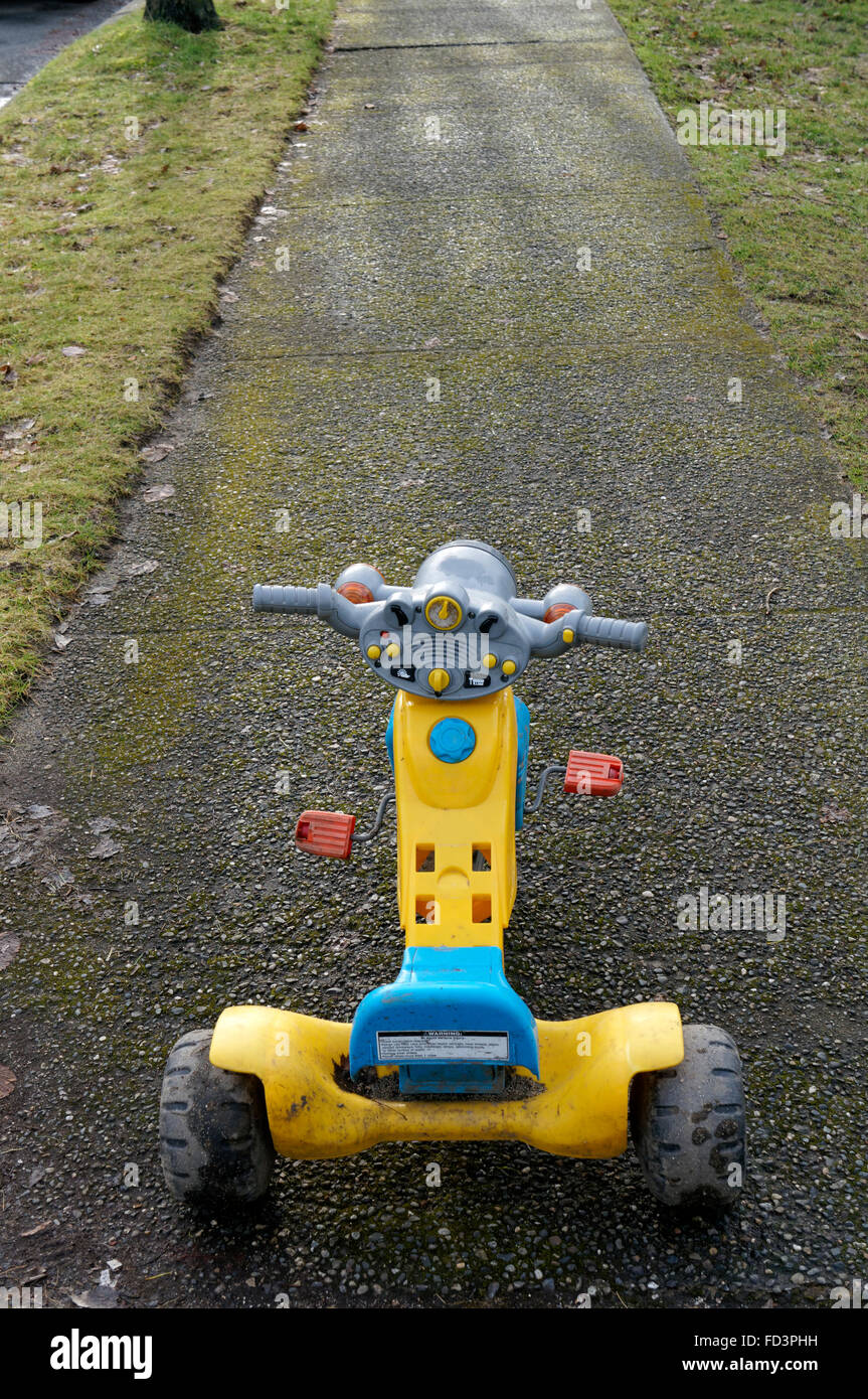 Child's toy plastic pedal powered motorcycle on the sidewalk Stock Photo