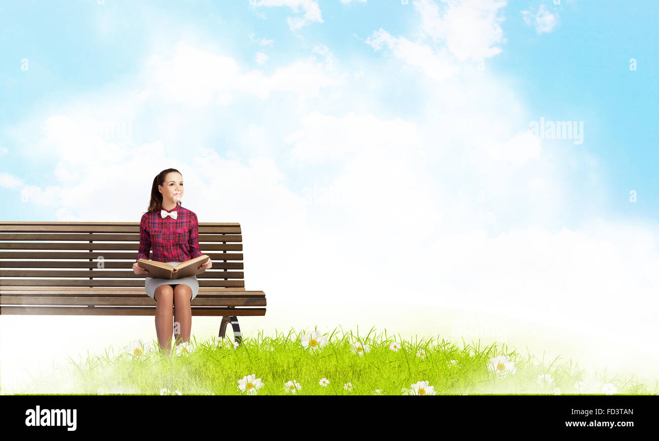Young woman sitting on bench and reading book Stock Photo - Alamy