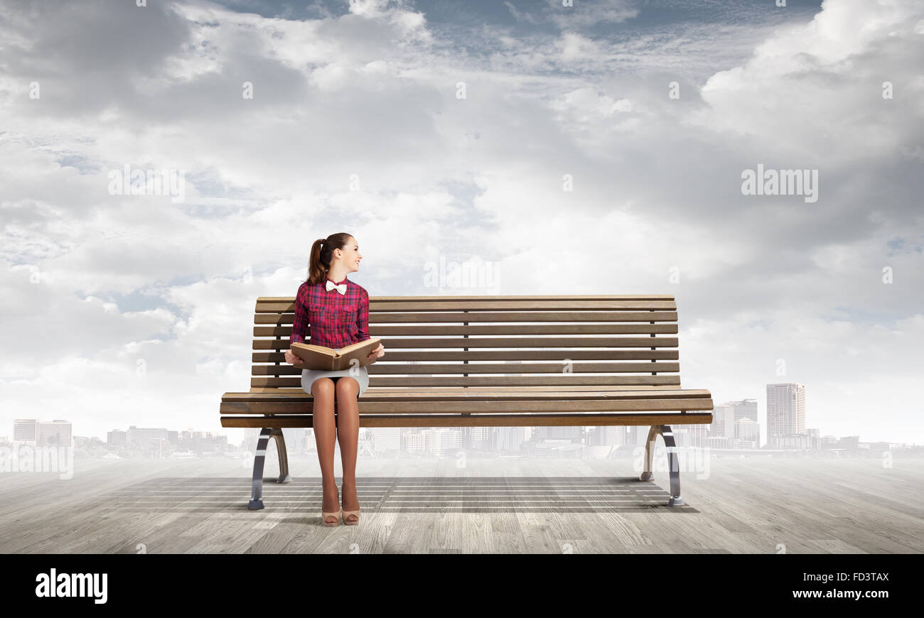 Young woman sitting on bench and reading book Stock Photo - Alamy