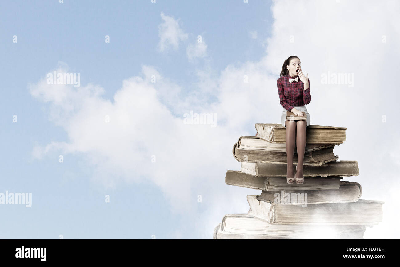 Young woman sitting on pile of books with book in hands Stock Photo - Alamy