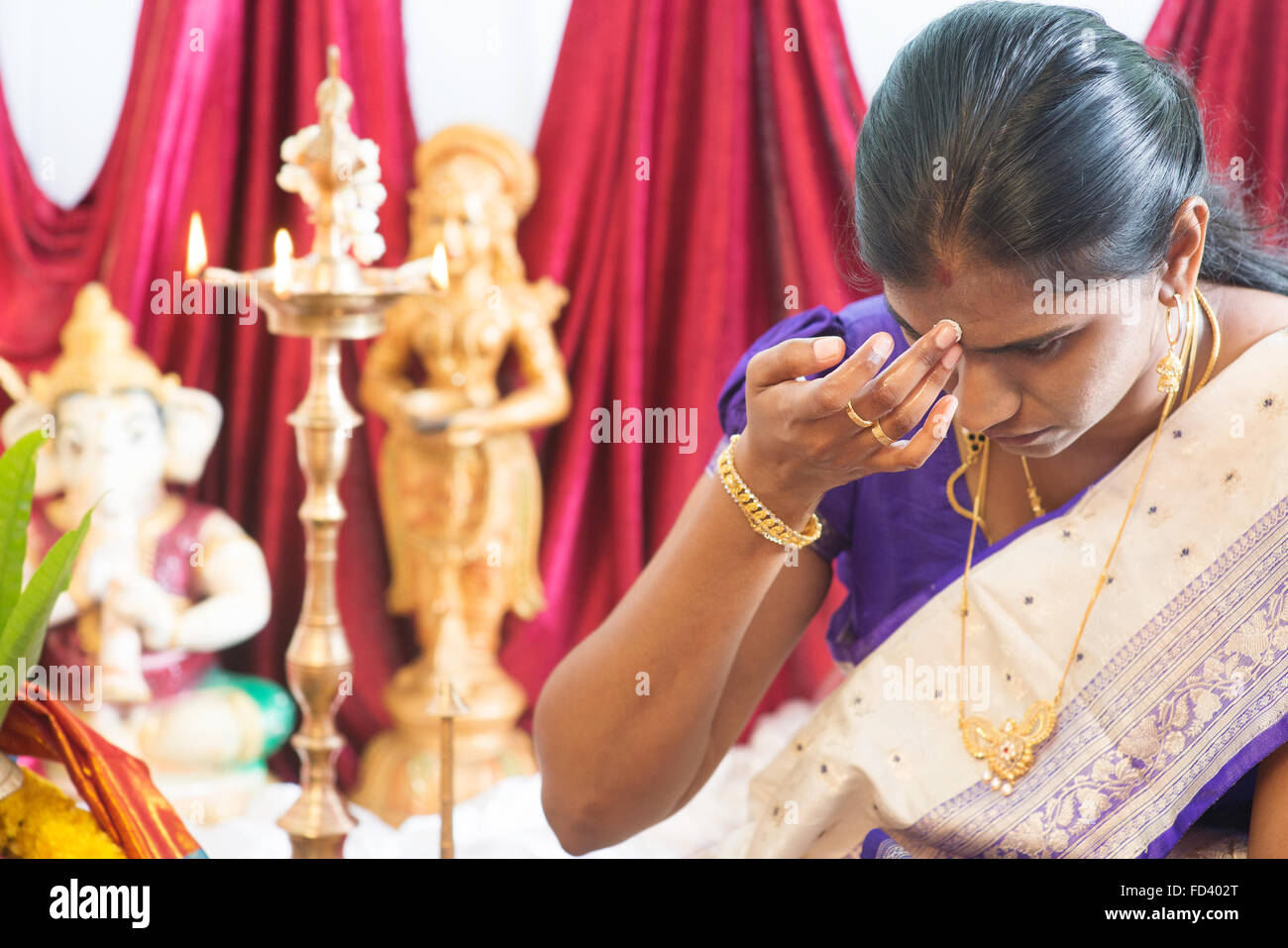 Hindu woman putting bindi or marking on her forehead during Indian traditional religious rituals, the tradition of Hinduism. Stock Photo