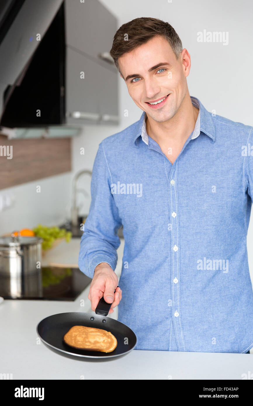 Portrait of handsome cheerful man making pancakes on the kitchen at