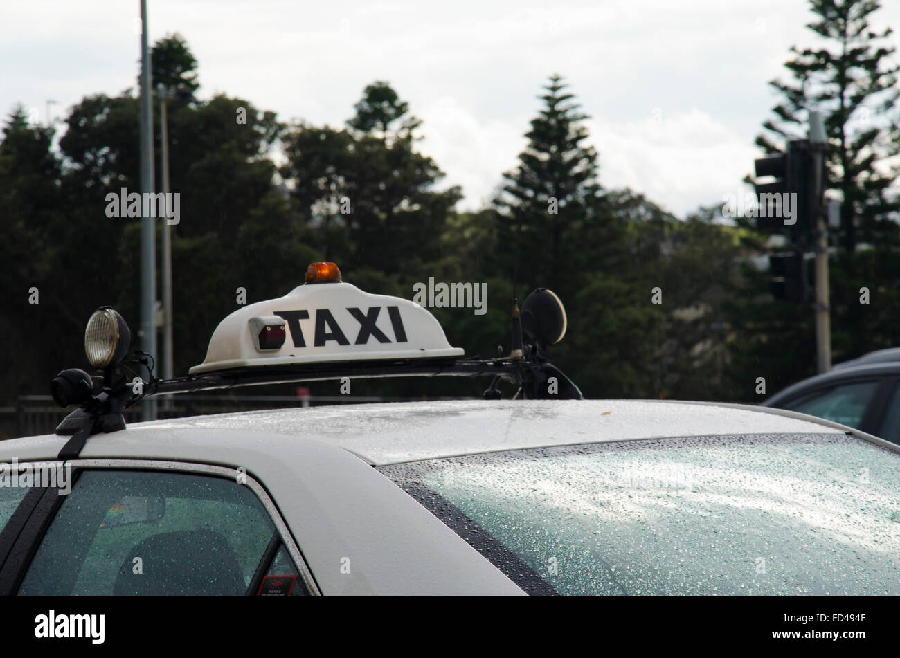 Viewed from behind with only the taxi sign and roof visible, a wet Sydney taxi stands waiting for a fare in the rain Stock Photo