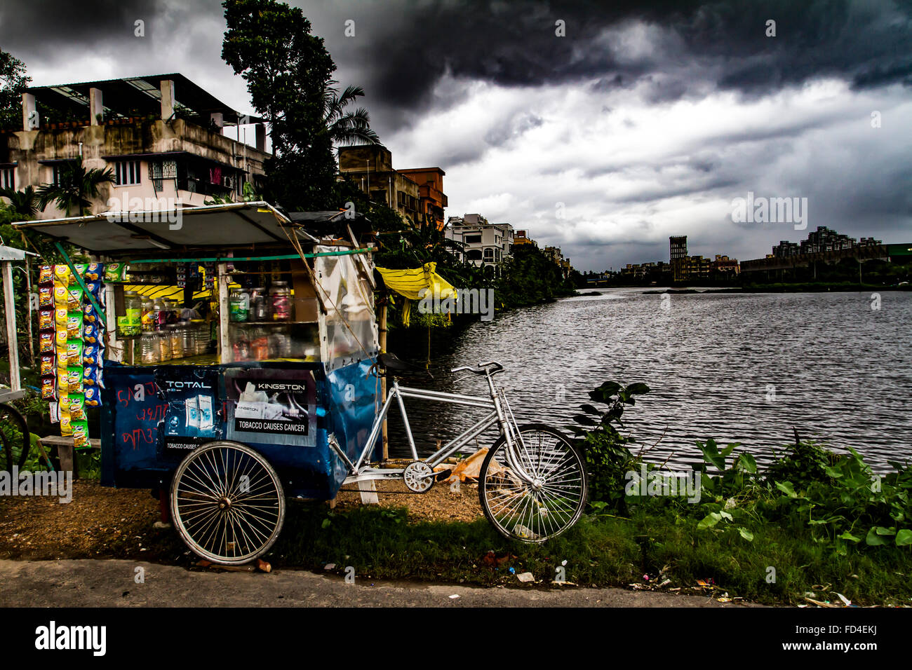 At the height of the Indian monsoon, a single Paan wallah cycle is set against a thunderous backdrop in Garia, Kolkata Stock Photo