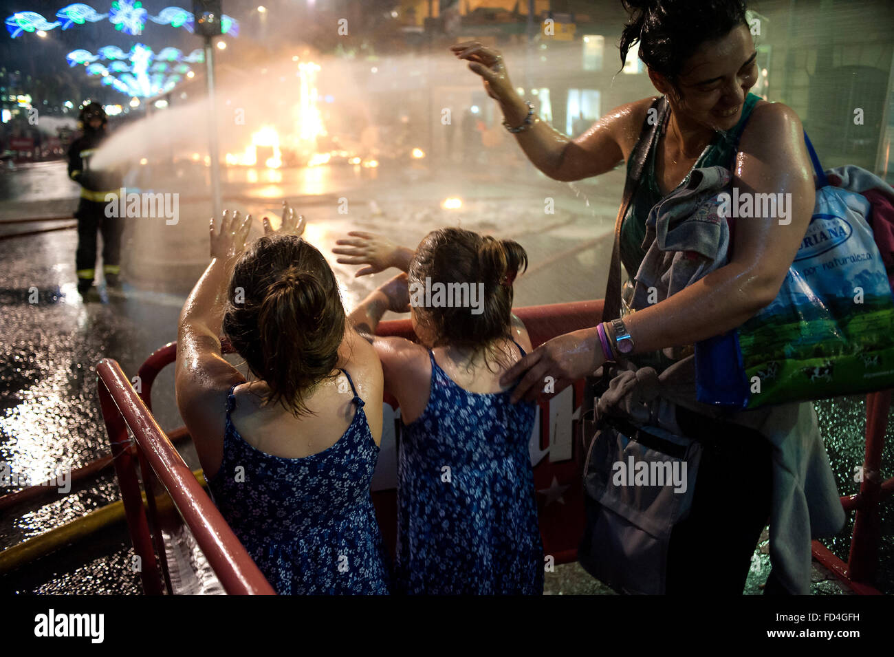 A firefighter wets a mother with her daughters during the night cremá the bonfires of San Juan. Stock Photo