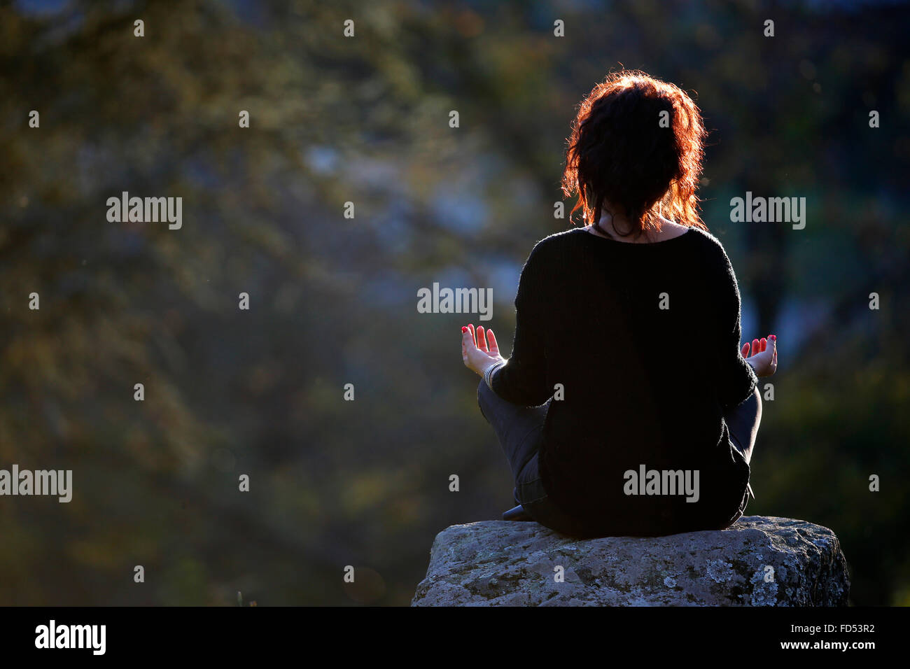 Woman sitting on a rock in Lotus Position. Stock Photo