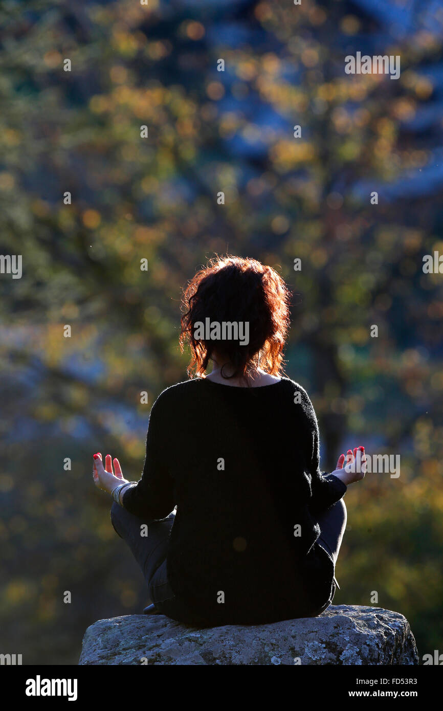 Woman sitting on a rock in Lotus Position. Stock Photo