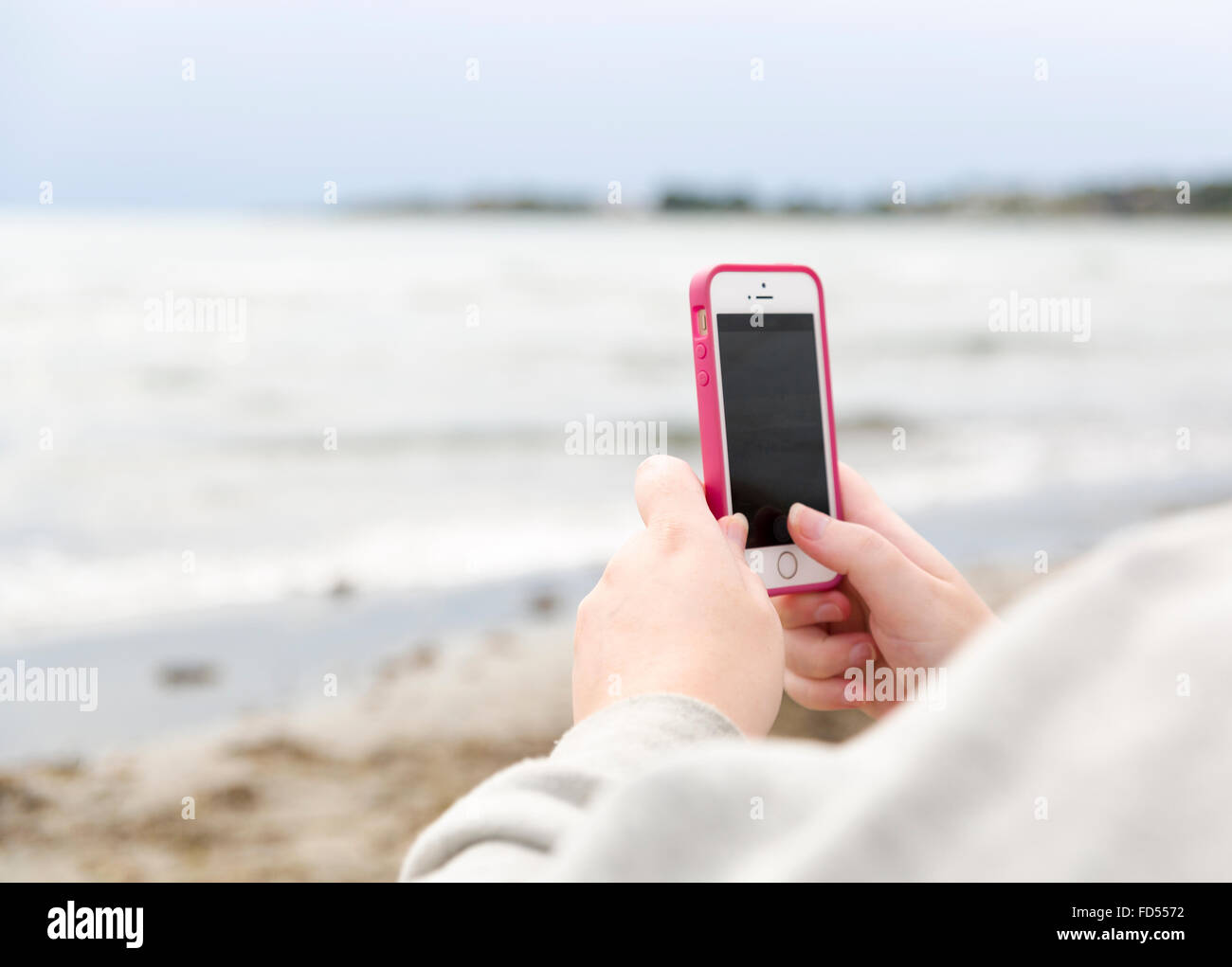 Woman taking a photo of the ocean with her modern white and pink smartphone  Model Release: Yes.  Property Release: No. Stock Photo