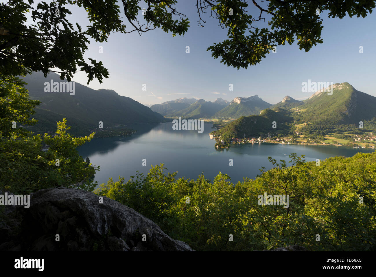 Southern Lake Annecy, rock faces and green forests of the Savoy mountains after sunrise in warm light Stock Photo