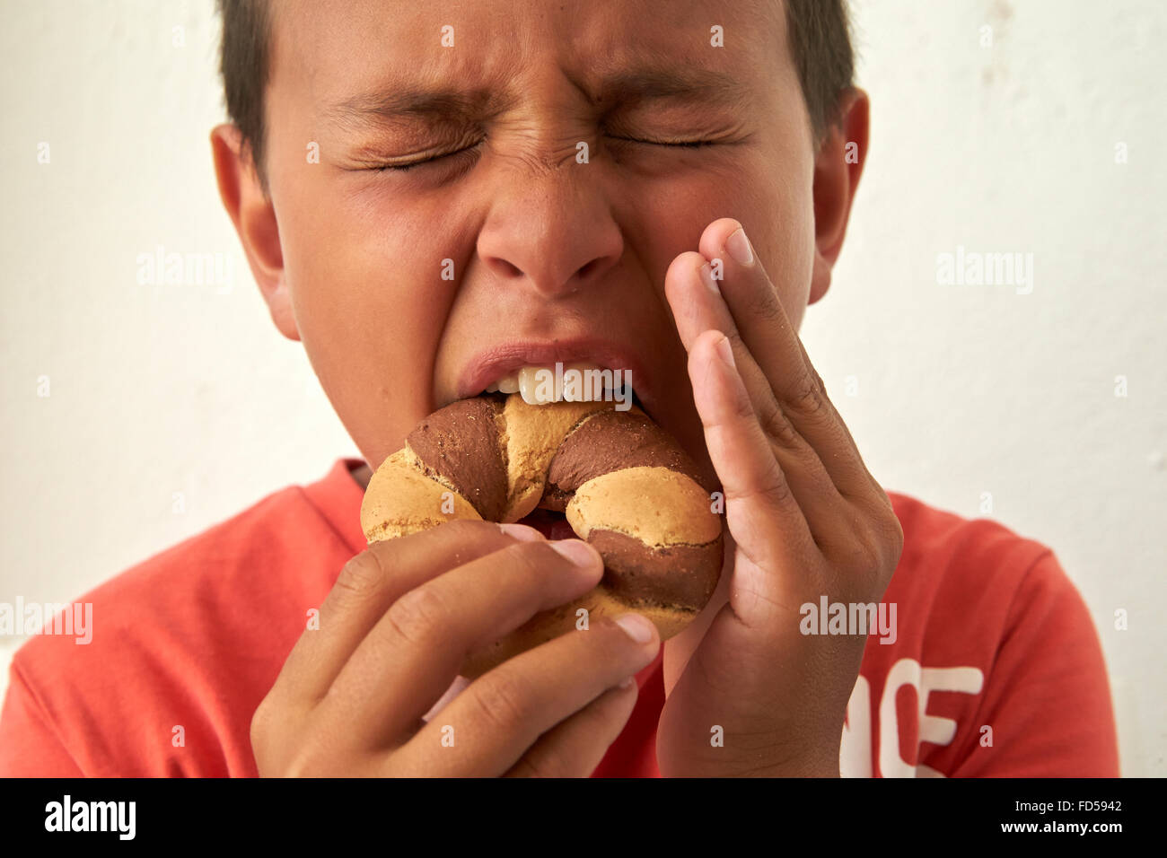Boy biting into a biscuit and hurting his teeth. Stock Photo
