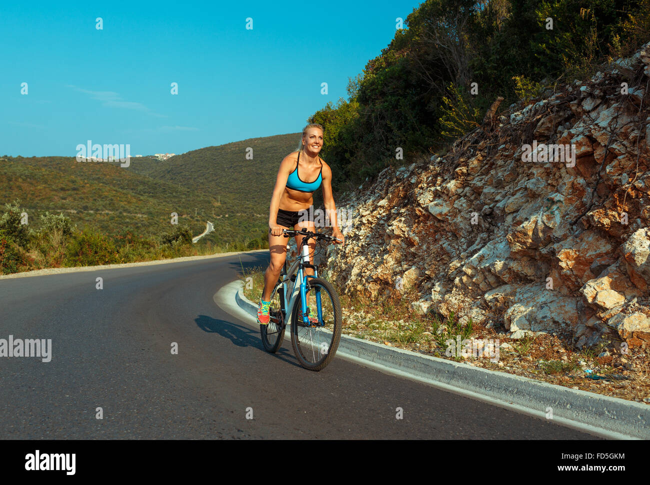 Happy woman cyclist riding a bike on a mountain road Stock Photo