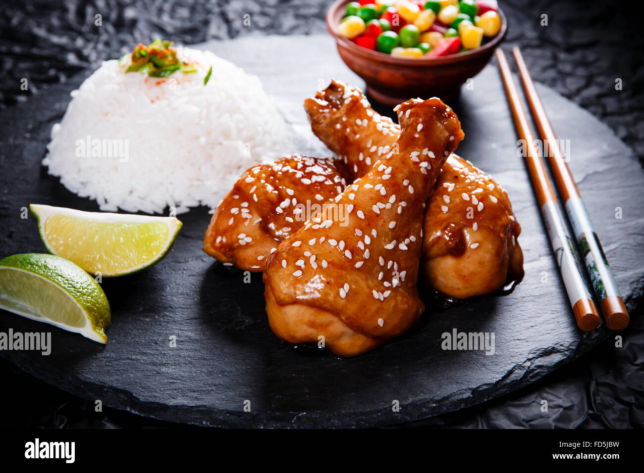Fried chicken legs with teriyaki sauce sesame seeds and rice on black stone Stock Photo