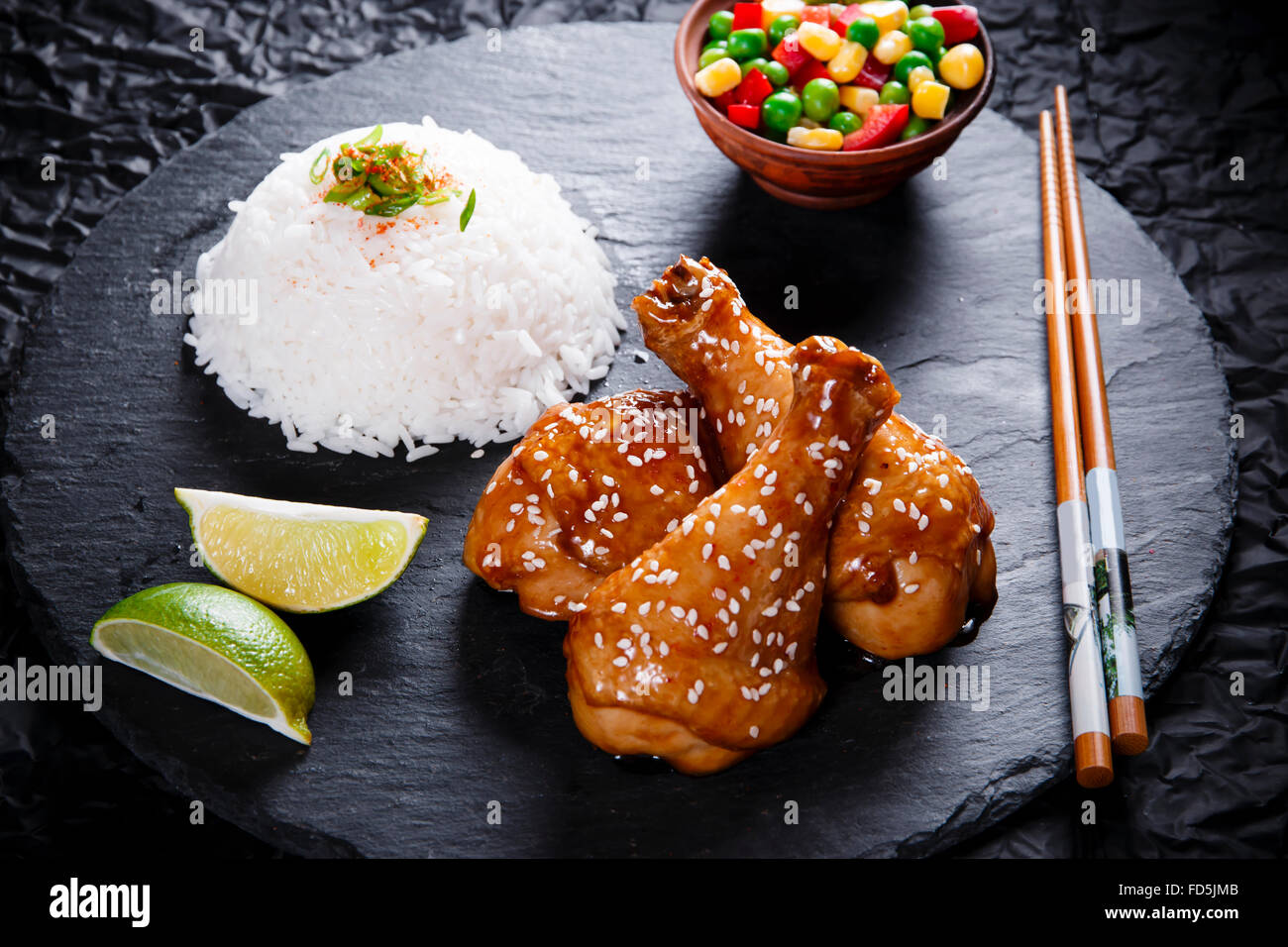 Fried chicken legs with teriyaki sauce sesame seeds and rice on black stone Stock Photo