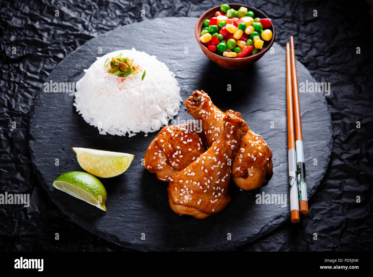 Fried chicken legs with teriyaki sauce sesame seeds and rice on black stone Stock Photo