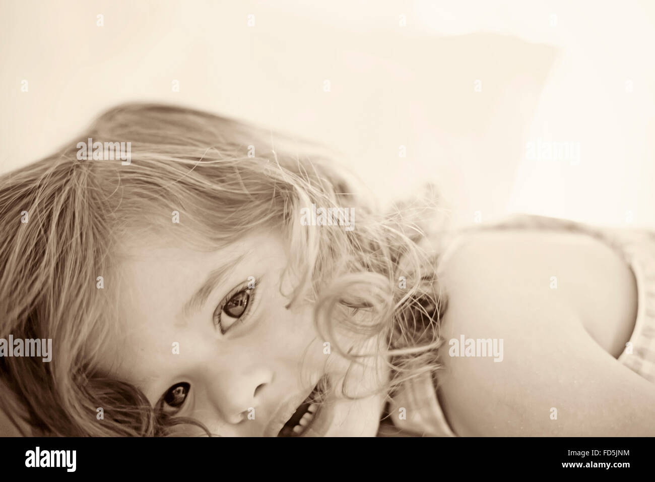 Beautiful toddler girl laying down looking at the camera with an interesting crop. Stock Photo