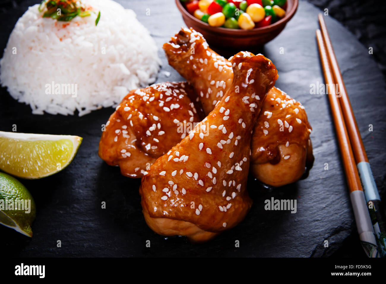 Fried chicken legs with teriyaki sauce sesame seeds and rice on black stone Stock Photo
